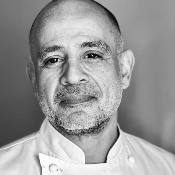Black and white portrait of a bald man with a beard wearing a chef's coat.