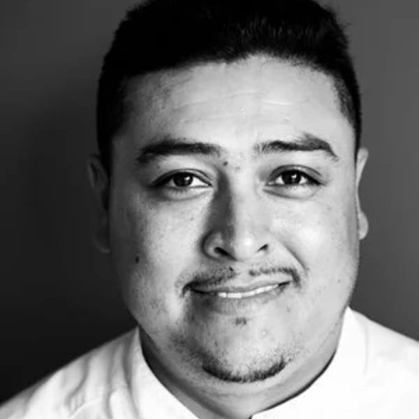 Black and white headshot of a smiling male chef with a goatee, wearing a white chef's coat.