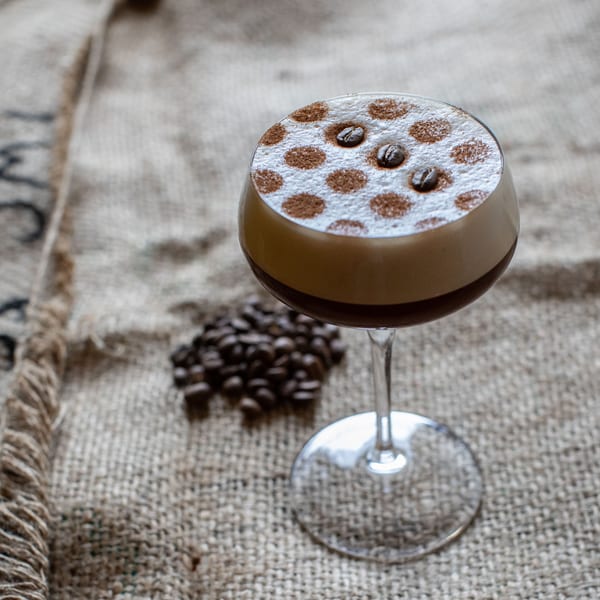 Espresso martini with coffee bean and cocoa powder garnish on a burlap surface with coffee beans.