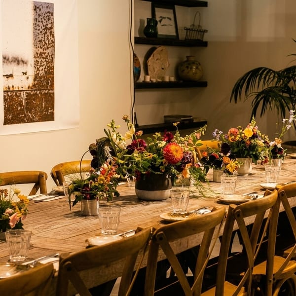 Long wooden dining table set with floral arrangements, glasses, and plates in a rustic restaurant.