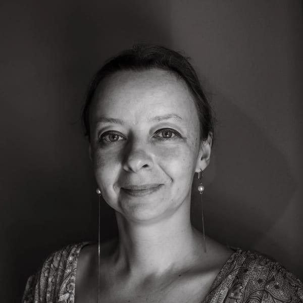 Black and white portrait of a smiling woman with long pearl earrings and a patterned top.