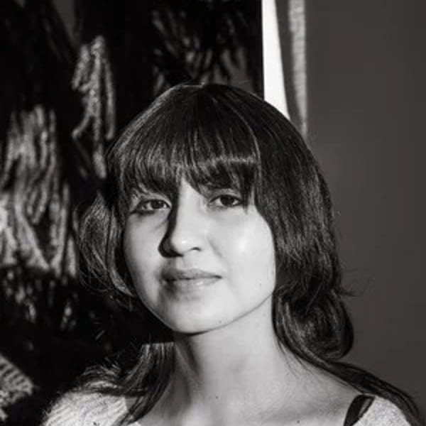 Black and white portrait of a woman with bangs, wearing a patterned sweater, looking forward.
