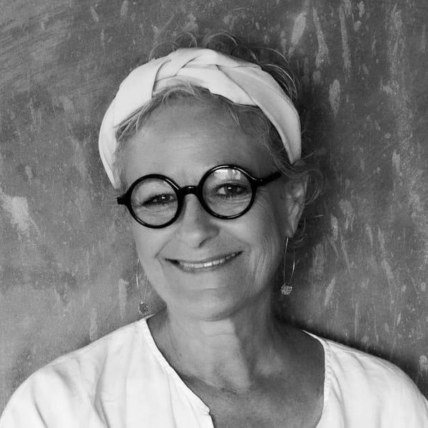Black and white portrait of a smiling woman with round glasses and a white headscarf.
