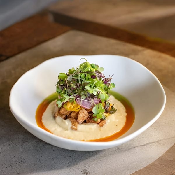Creamy dish with microgreens, crispy bits, and red onion in a white bowl.