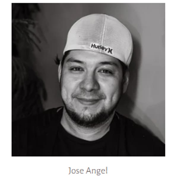 Black and white portrait of Jose Angel, smiling and wearing a Hurley baseball cap.