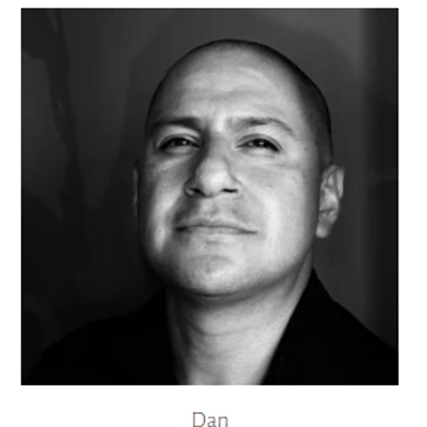 Black and white headshot of a man with a shaved head looking directly at the camera.