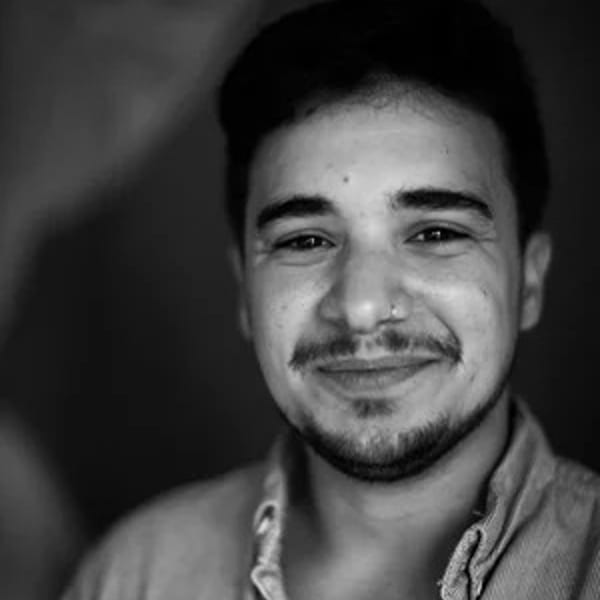 Black and white portrait of a smiling man with a nose ring and beard looking at the camera.