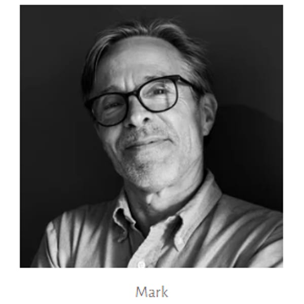 Black and white headshot of a man named Mark, wearing glasses and a collared shirt.
