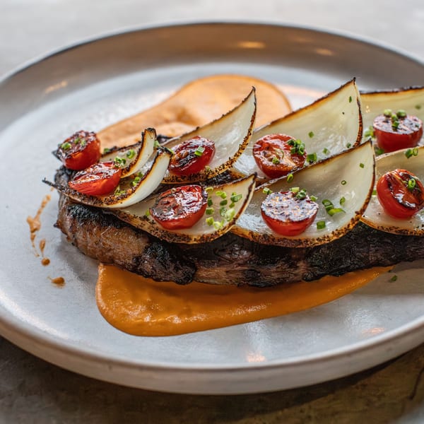 Grilled steak with caramelized onions, roasted cherry tomatoes, and chives on an orange sauce.