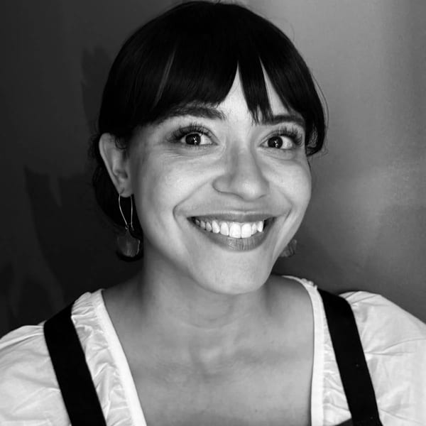 Black and white portrait of a smiling woman with dark hair and bangs, wearing an apron.