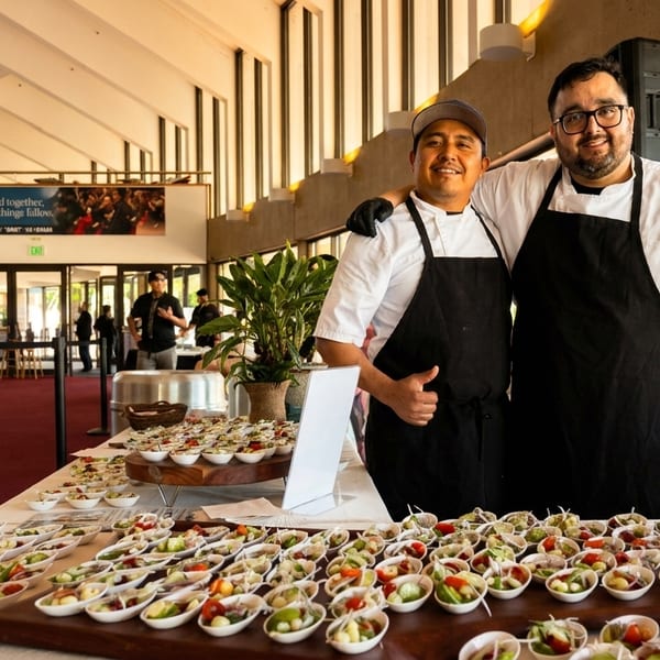 Two chefs stand proudly behind a table laden with numerous small appetizer servings at an event.