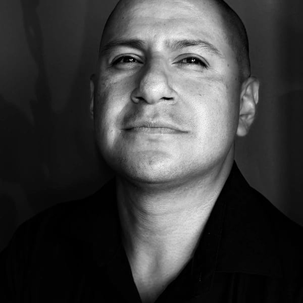 Black and white portrait of a man with a shaved head, wearing a dark collared shirt.